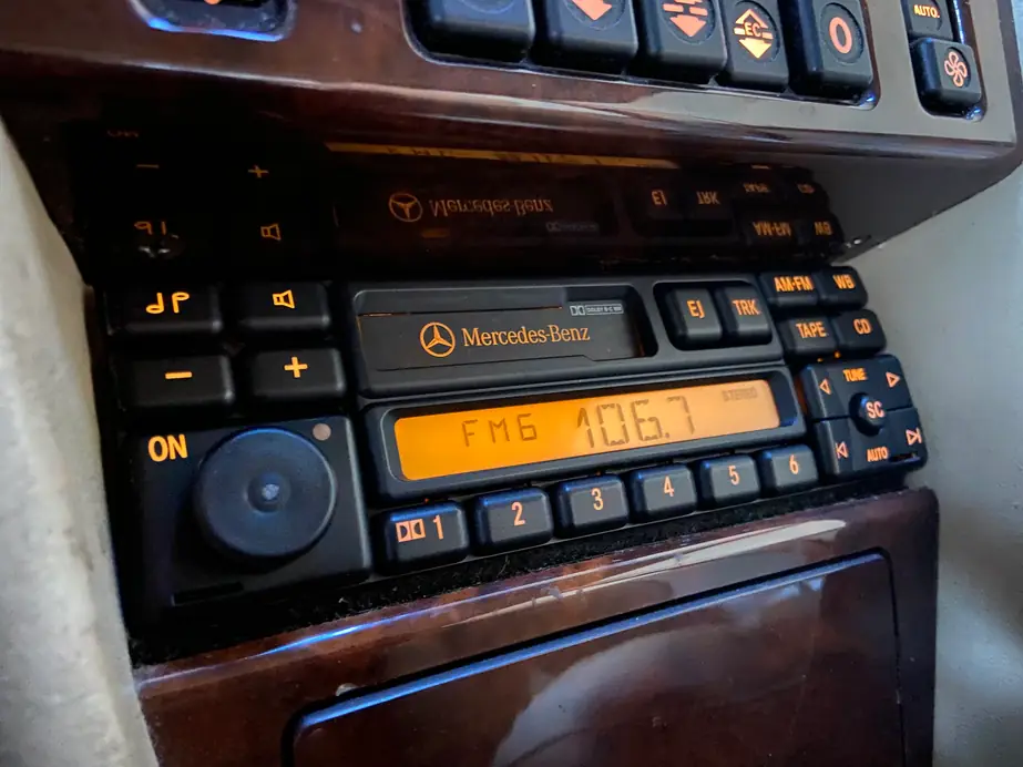 A Mercedes-Benz factory radio powered on in a wood-trim dashboard, tuned to FM 106.7